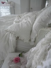 a white shabby chic bedroom with refined furniture, white lace and ruffle bedding and floral touches