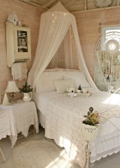 a neutral and pastel shabby chic bedroom with a white forged bed, a canopy, a forged screen, lace, floral and doily textiles looks ethereal