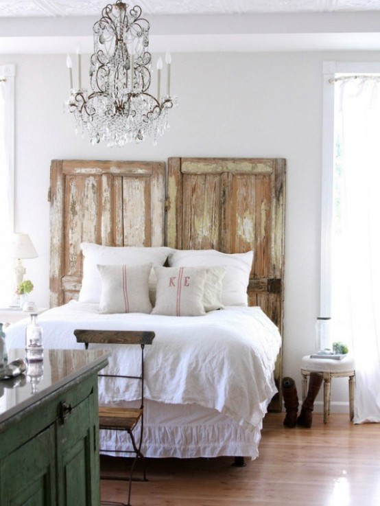 a shabby chic farmhouse bedroom with refined rustic furniture, a crystal chandelier, shabby doors to instead of a headboard