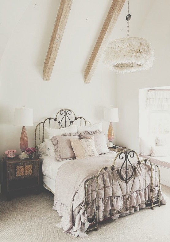 a neutral vintage bedroom with wooden beams, a forged bed with grey and white bedding with ruffles and chic nightstands