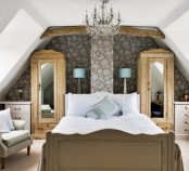 a bedroom done with vintage touches – a floral statement wall, chic furniture, a vintage crystal chandelier and wooden beams on the ceiling
