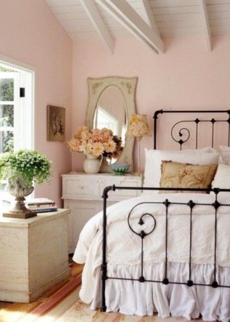 a blush vintage bedroom with neutral furniture, a forged bed, a mirror and some greenery and dried bloom arrangements