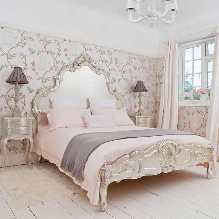 a pastel and neutral vintage bedroom with a floral wallpaper wall, refined vintage furniture, a chic chandelier and grey and pink bedding