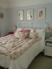 a vintage pastel bedroom with light blue walls, a metal bed and vintage furniture, floral artworks and floral bedding for a cute touch