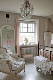 a refined vintage bedroom with grey walls, elegant furniture, a forged bed, a refined neutral chair and a crystal chandelier