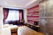 a colorful contemporary teen bedroom with purple curtains, a striped accent wall, an elegant white sofa, a sheer wardrobe with sliding doors
