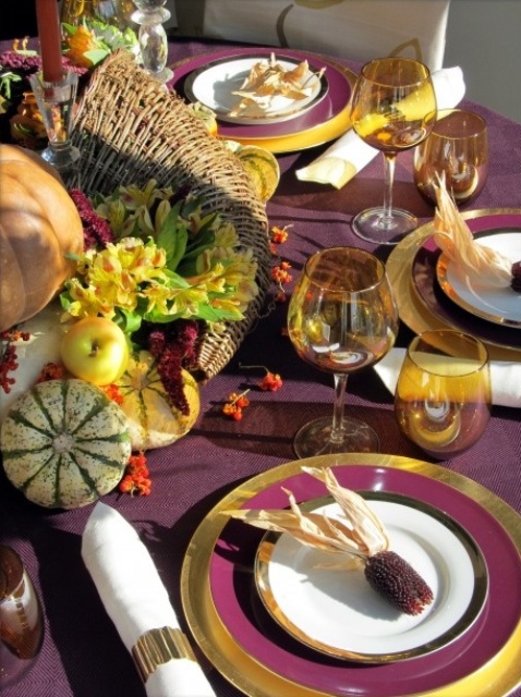 a bold rustic Thanksgiving tablescape with a purple tablecloth and plates, a cornucopia, some leaves, pumpkins, berries and corn cobs