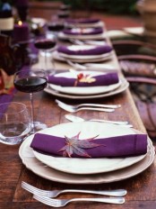 a chic Thanksgiving tablescape with an uncovered table, a purple table runner and napkins plus deep purple candles and bold fall leaves is amazing