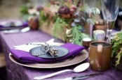a bright purple Thanksgiving tablescape with a purple tablecloth and napkins, greenery and purple blooms is a stylish idea for a woodland Thanksgiving party