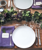 a chic Thanksgiving tablescape with a greenery runner, purple napkins and berries, white porcelain and chic cutlery is amazing