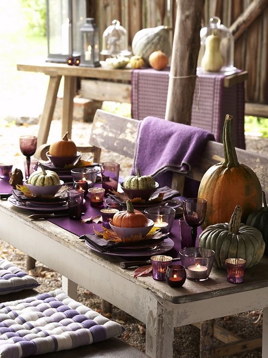 a rustic Thanksgiving tablescape with a purple table runner, napkins, glasses and candle holders, large natural pumpkins and towels