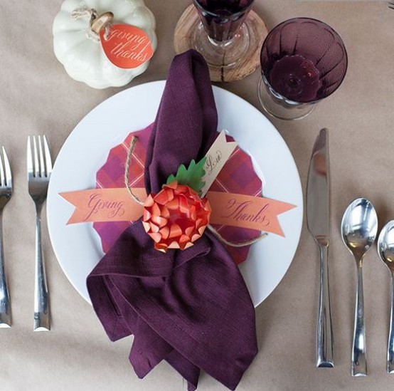 a simple Thanksgiving place setting with a grey tablecloth, a purple menu and napkin, purple glasses and a white pumpkin