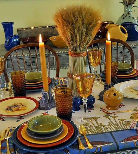 a colroful fall table setting with bright porcelain, candles , wheat and blue porcelain candle holders and plates for a bolder look