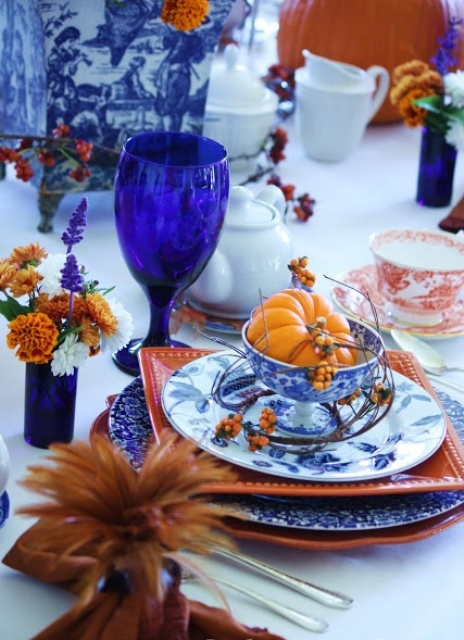 a bright and elegant Thanksgiving tablescape with orange and blue and white plates, bold blue glasses, blooms and berries