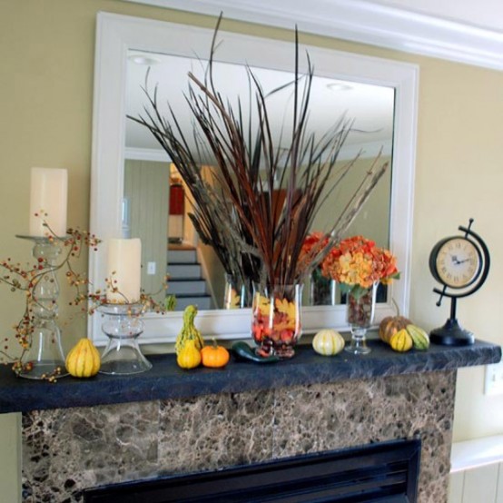 a modern rustic Thanksgiving mantel with bright gourds and pumpkins, with a feather and dried leaf vase and bold blooms and candles