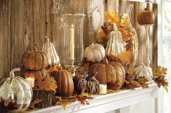 a neutral and rustic Thanksgiving mantel with tree stumps, fall leaves, pumpkins stacked and gourds, candles in a vase and an oversized vase with leaves