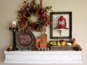 a simple rustic Thanksgiving mantel with a faux flower and berry wreath, a crate with faux veggies and fruits, wooden pumpkins and a chalkboard sign