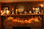 a beautiful vintage and rustic Thanksgiving mantel with white stands, vases, white pumpkins, candles and a light and leaf garland under it