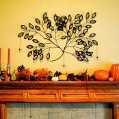 a fall or Thanksgiving mantel with bold pumpkins, dried leaves, pinecones, and a string tree art piece on the wall