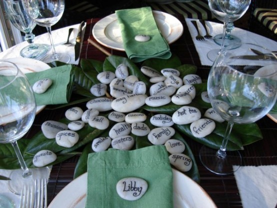 a simple Thanksgiving tablescape with green leaves and napkins, with pebbles that tell you what to sya thanks for