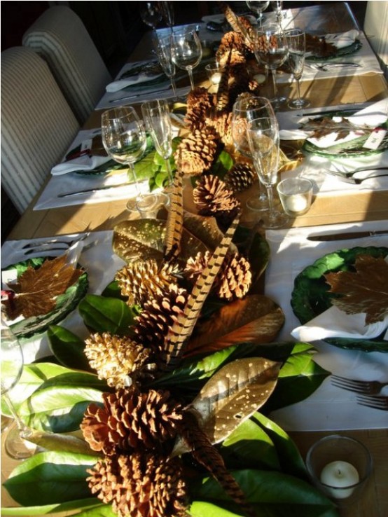 a natural Thanksgiving tablescape with green plates, a cool leaf runner with feathers and pinecones, gilded leaves accenting each place setting
