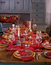 a colorful Thanksgiving tablescape with bold red linens, gold and silver chargers, faux berries and leaves and tall and thin candles is amazing