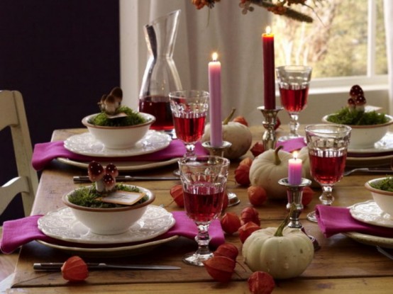 a colorful woodland-themed Thanksgiving tablescape with hot pink napkins, a hot pink and burgundy candle, mushrooms, moss and some dried seed pods and gourds is awesome