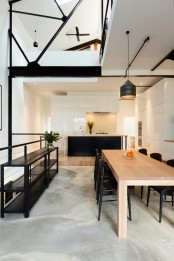 a minimal dining room with a light-stained table, black chairs, a black storage unit, black pendant lamps and some greenery