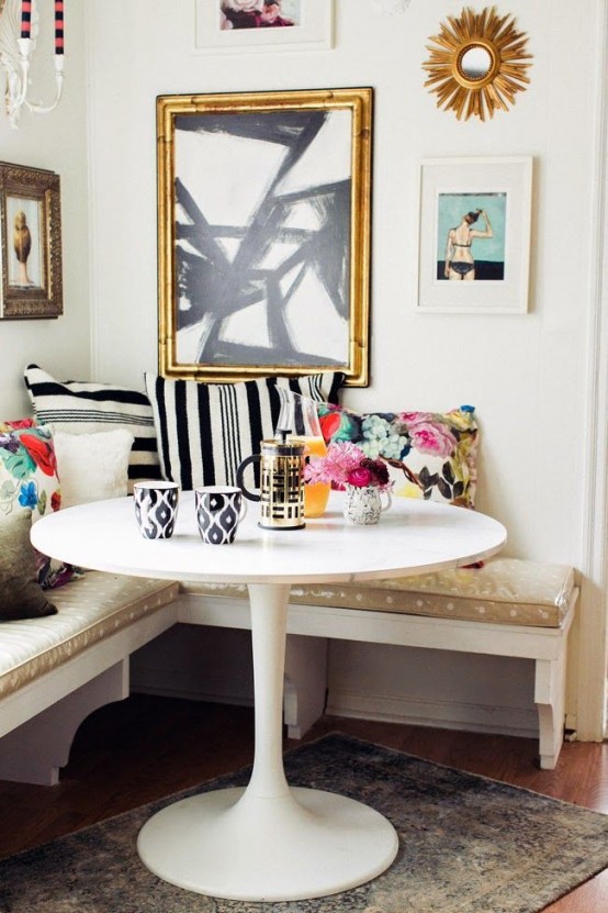 a glam eclectic dining space with a corner bench, a round table, printed and colorful pillows, a statement gallery wall and a neutral rug