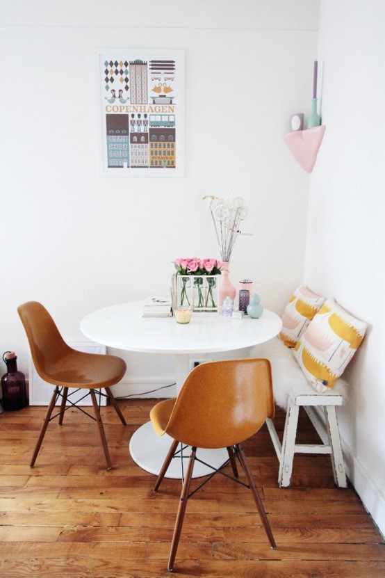 a cool and chic dining area with a bench with printed pillows, a white round table, leather chairs, some blooms and pastel accessories