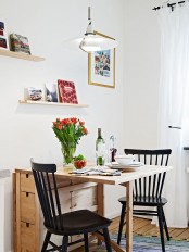 a small and cozy dining space with a folding table, black chairs, open shelves, books and artworks is cozy space