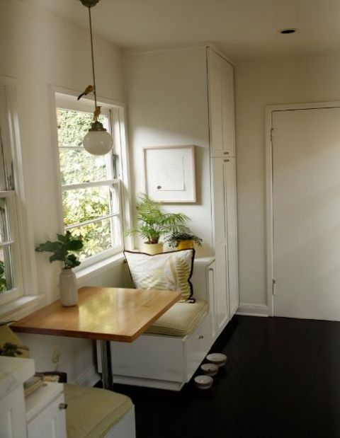a tiny dining space with a small table and two built in seats by the window plus potted greenery around is wow
