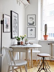 a small Nordic dining area with a folding table, vintage white chairs, a black and white gallery wall and some plants