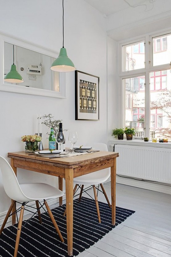 a tiny Scandinavian dining zone with a wooden table, white chairs, a printed rug, a pendant lamp and lots of greenery