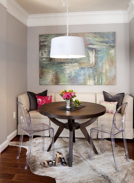 a chic small dining space with a touch of glam, a neutral sofa with pillows, a dark stained table, ghost chairs, an abstract artwork and a rug