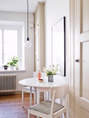 a little Nordic dining space with a round table, striped chairs and a pendant bulb plus a statement artwork is a cozy nook to have a meal