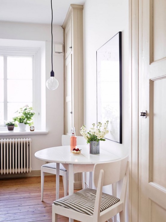 a little Nordic dining space with a round table, striped chairs and a pendant bulb plus a statement artwork is a cozy nook to have a meal