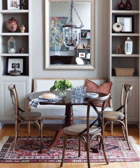 a tiny refined vintage dining nook with a white bench, a dark stained table, matching chairs, printed pillows and a pendant lamp