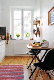 a tiny dining space in a Scandinavian kitchen, with a small folding table and black chairs, open shelves and an artwork