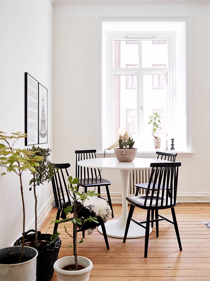 a small and cool Scandinavian dining nook with a white round chair, vintage black chairs, a black and white gallery wall and potted plants