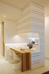 a modern built-in dining space with a built-in lighting fixtures, a wooden table, white sculptural chairs and a large vase