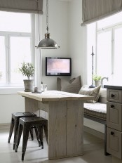 a Scandi industrial dining space with a bench, a rough wooden table, metal stools, a metal pendant lamp and printed pillows