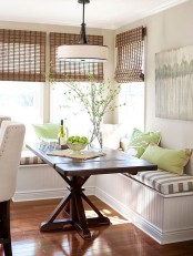 a cozy farmhouse dining space with a corner bench with cushions and pillows, a stained wooden table, blooming branches and a pendant lamp