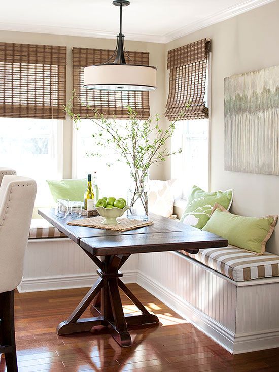 a cozy farmhouse dining space with a corner bench with cushions and pillows, a stained wooden table, blooming branches and a pendant lamp