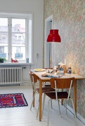 a Scandinavian dinign space with a plywood table and chairs, a wallpaper accent wall and a vintage red pendant lamp