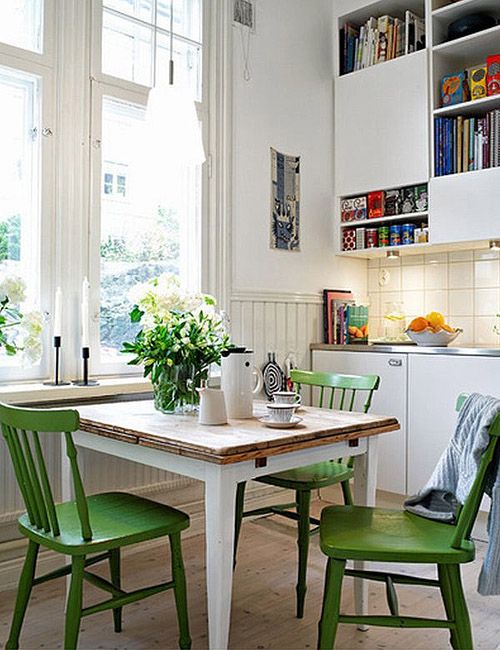 a lovely small dining zone with a small dining table, green chairs, some blooms and candles and a pendant lamp
