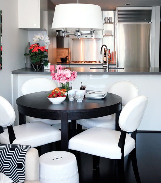a chic modern dining zone with a black round table, white chairs, a pendant lamp and some pink blooms is lovely