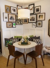 a corner bench with lots of printed pillows, a round table, dark stained chairs, a large gallery wall and a pendant lamp