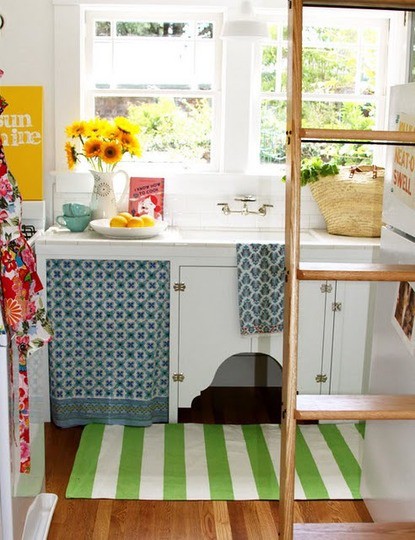 a tiny cottage kitchen with white cabinets, printed colorful texitles, a ladder for storing things up and on it