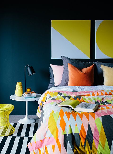 a bedroom with a black accent wall, a bed with super colorful geometric print bedding, a striped rug and a yellow and white table
